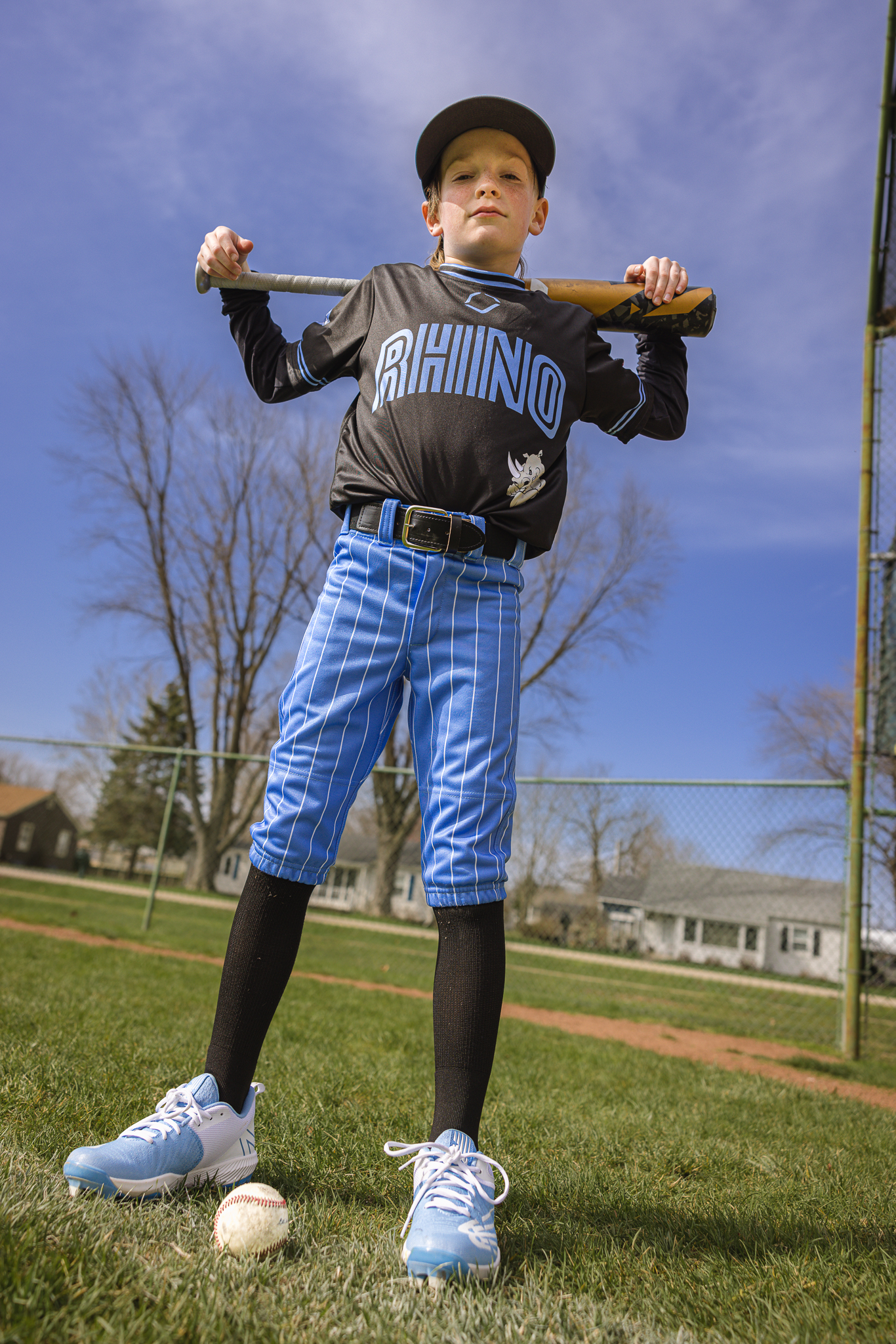 boy in baseball uniform standing tall with bat over his shoulders and looking down at camera at Channahon Pony Baseball Fields in Channahon, IL