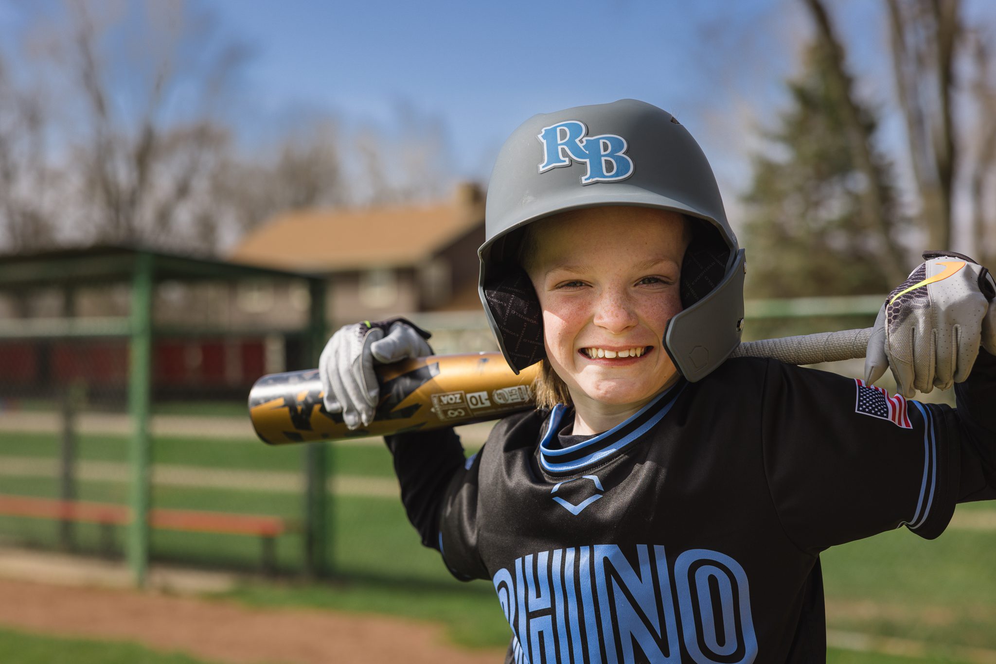 boy in baseball uniform smiling at the camera while holding his bat over his shoulders at Channahon Pony Baseball Fields in Channahon, IL