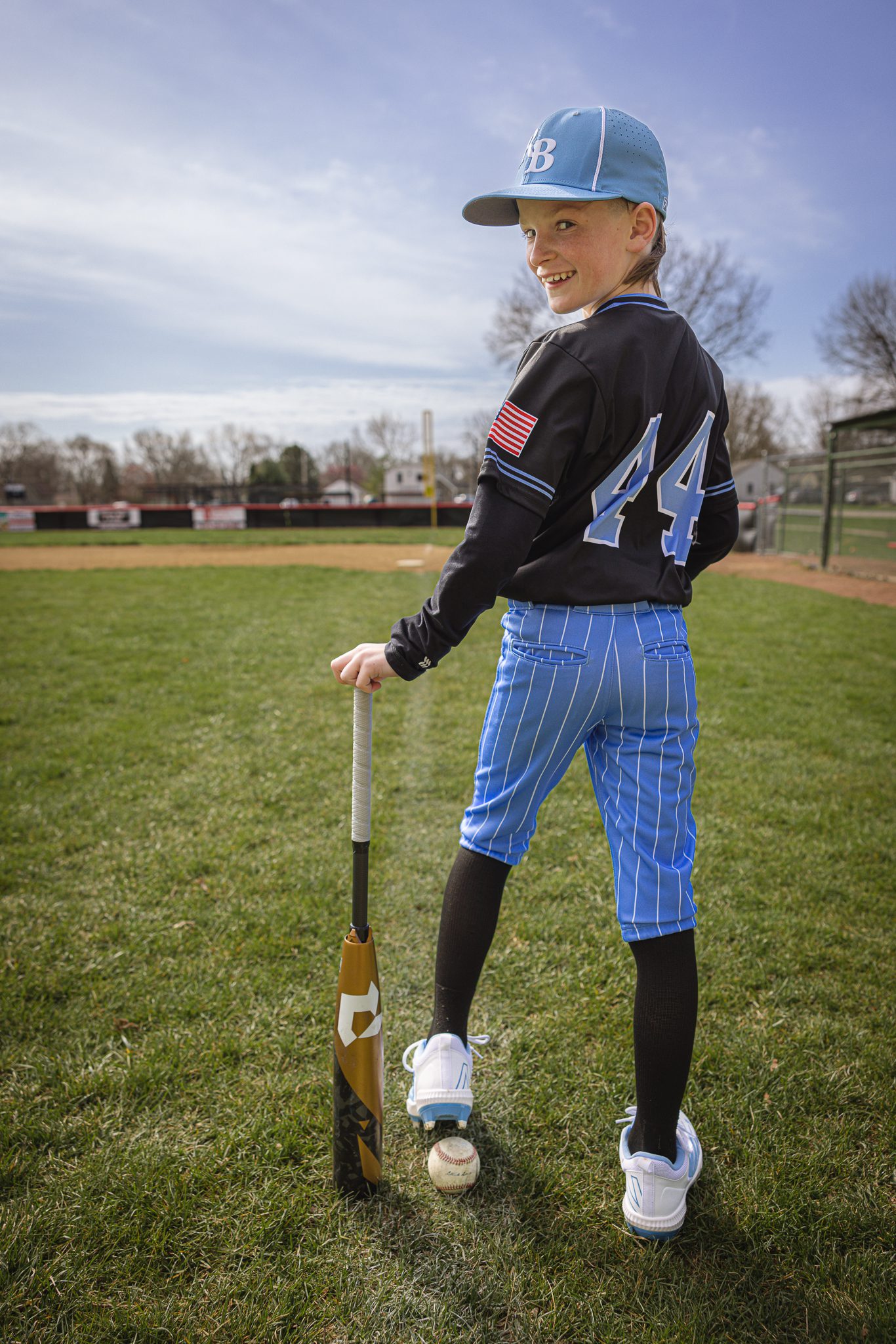 Boy turned opposite direction with cleat on top of ball and holding bat and turned over his shoulder looking at me while at Channahon Pony Baseball Fields in Channahon, IL