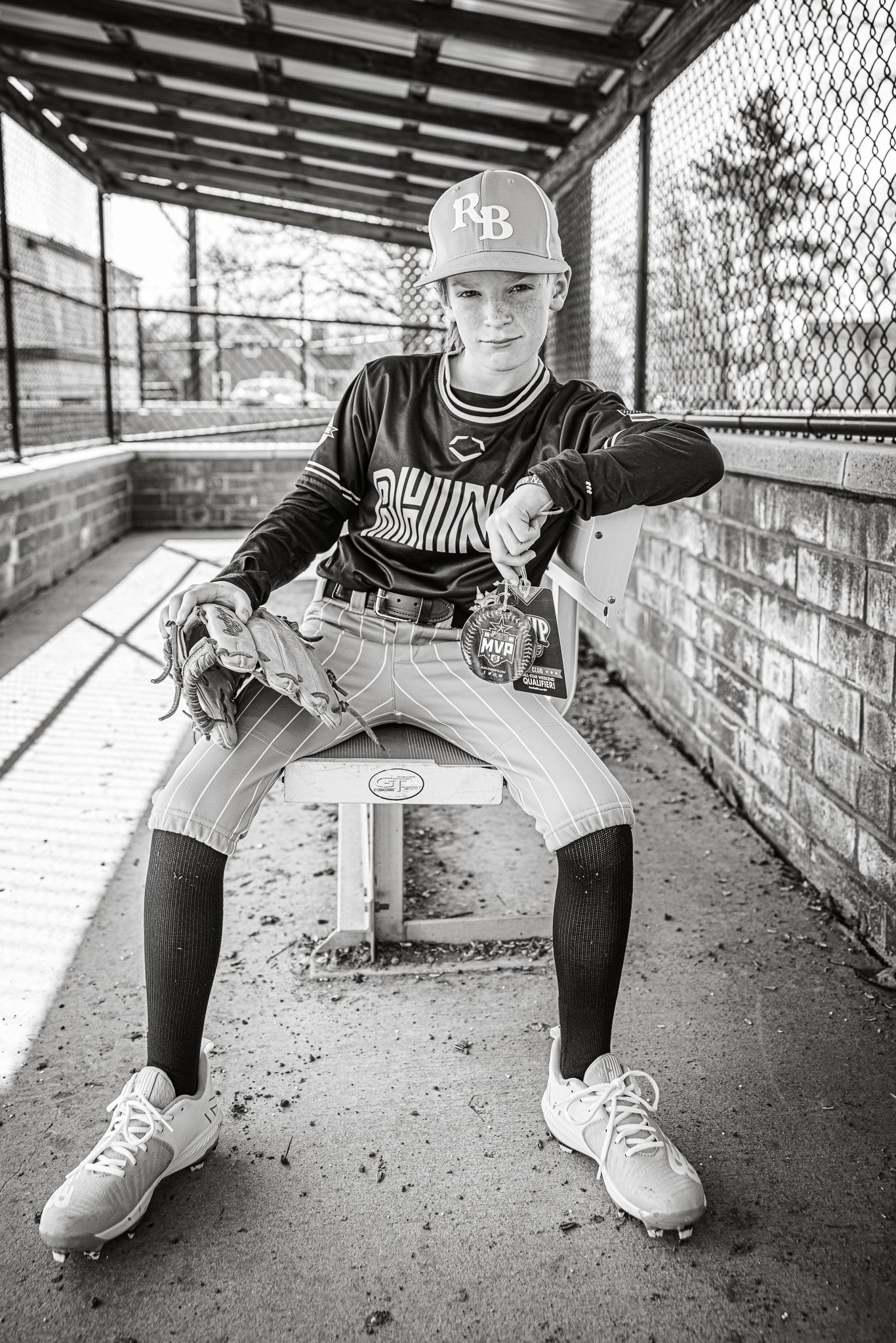 Boy in baseball uniform showing off his MVP badges while sitting in the dug out at Channahon Pony Baseball Fields in Channahon, IL