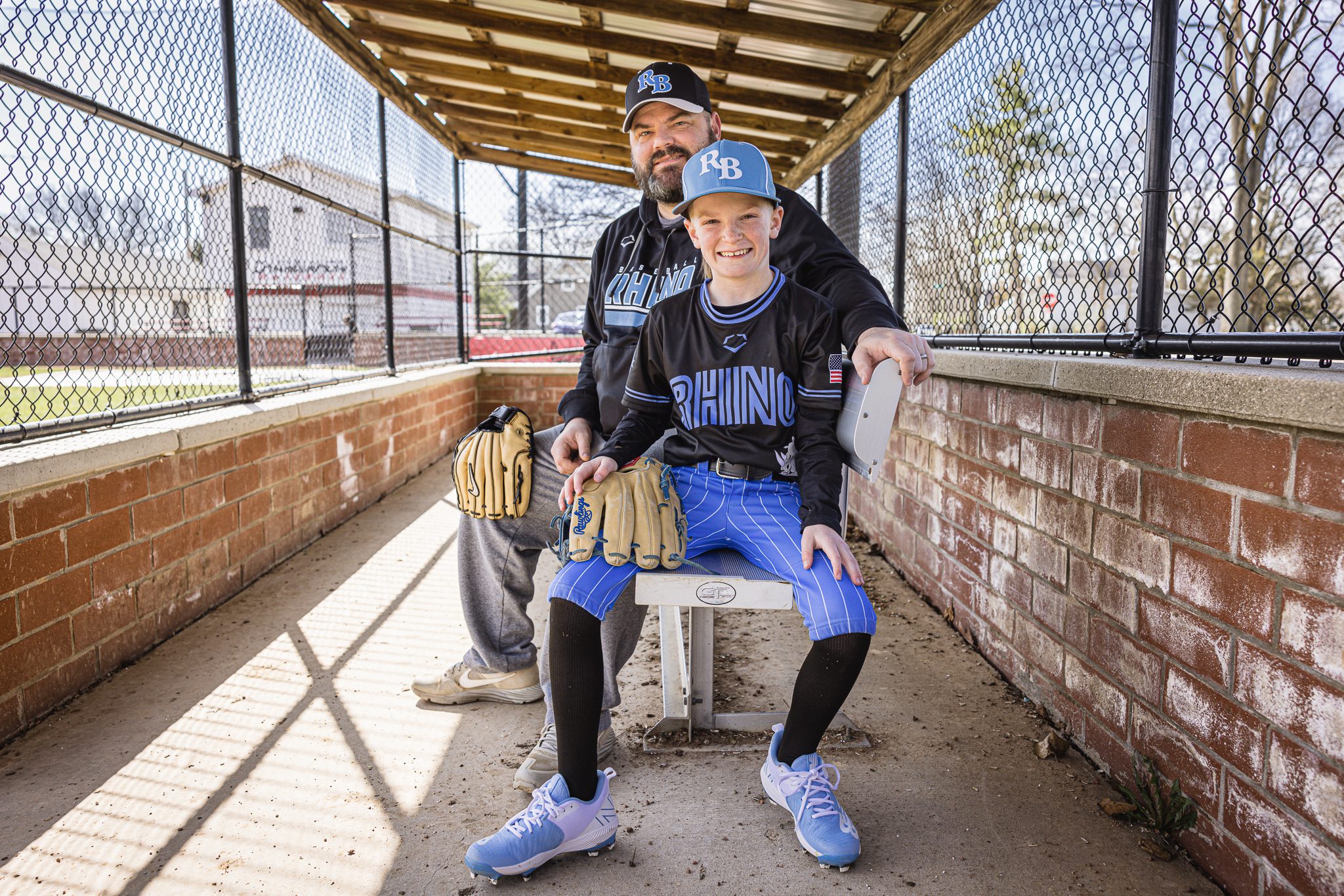 Dad and son sitting in brick dug out and smiling at camera at Channahon Pony Baseball Fields in Channahon, IL