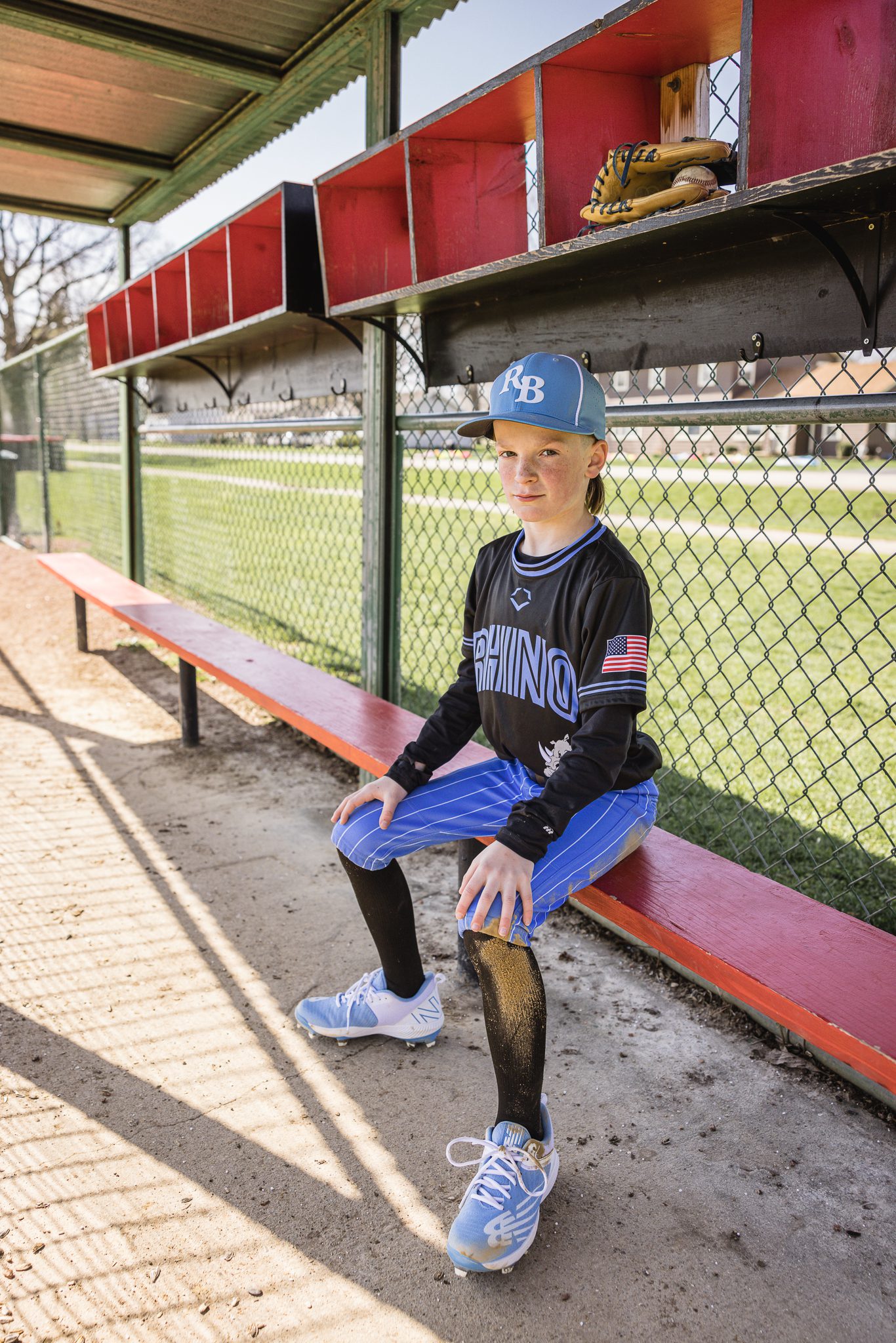 Boy in baseball uniform looking fierce while sitting on red bench ball in the dug out at Channahon Pony Baseball Fields in Channahon, IL