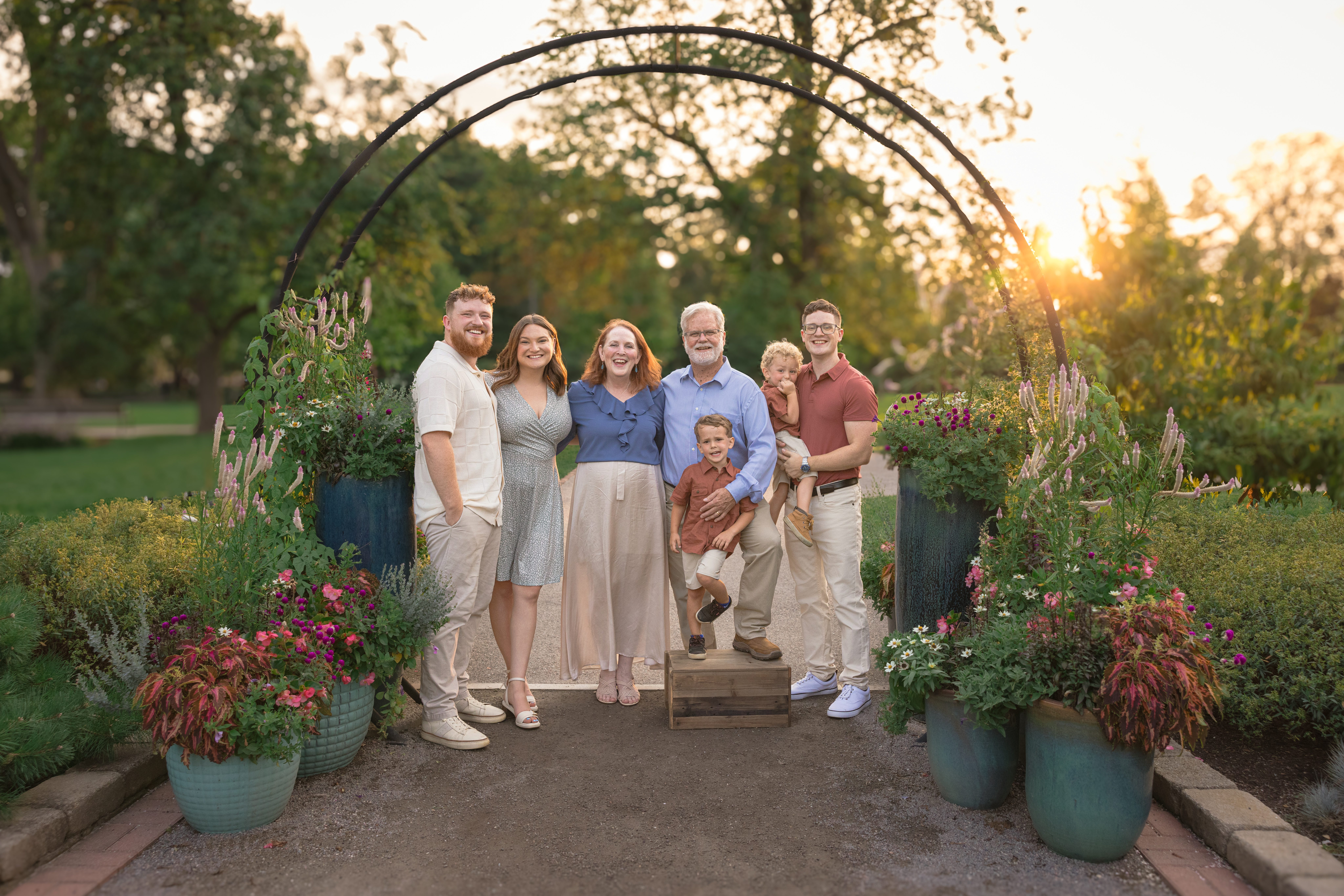 Extended family of seven standing and posing for the camera under a large black arch during a family photography session at Cantigny Park in Wheaton, IL