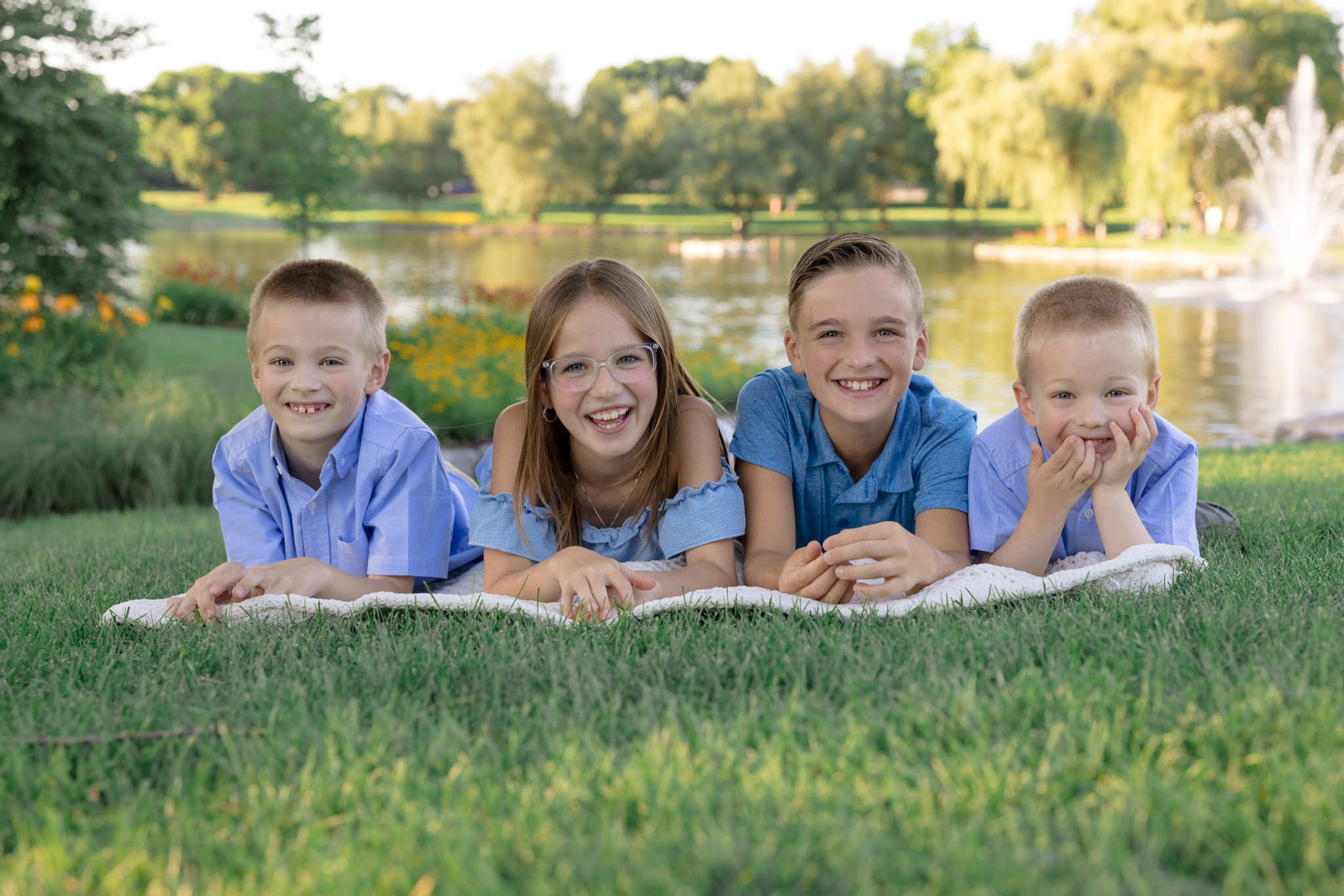 Four younger cousins lying on their bellies on top of a blanket all looking and smiling at the camera. Taken during an extended family photography session in the western suburbs of Chicago.