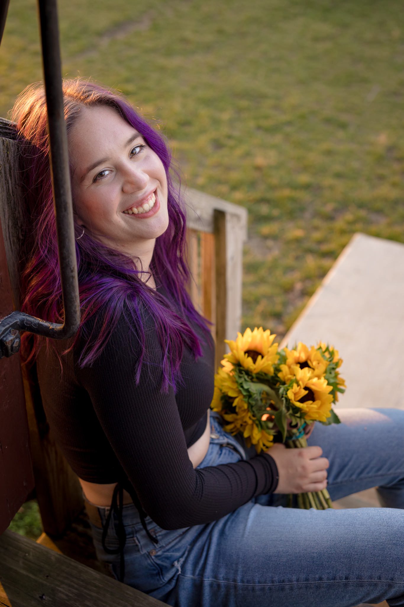Teenage female sitting on a set of stairs and looking up at the camera while holding a bouquet of sunflowers. Photo taken during graduating senior session at St James Farm in Warrenville, IL