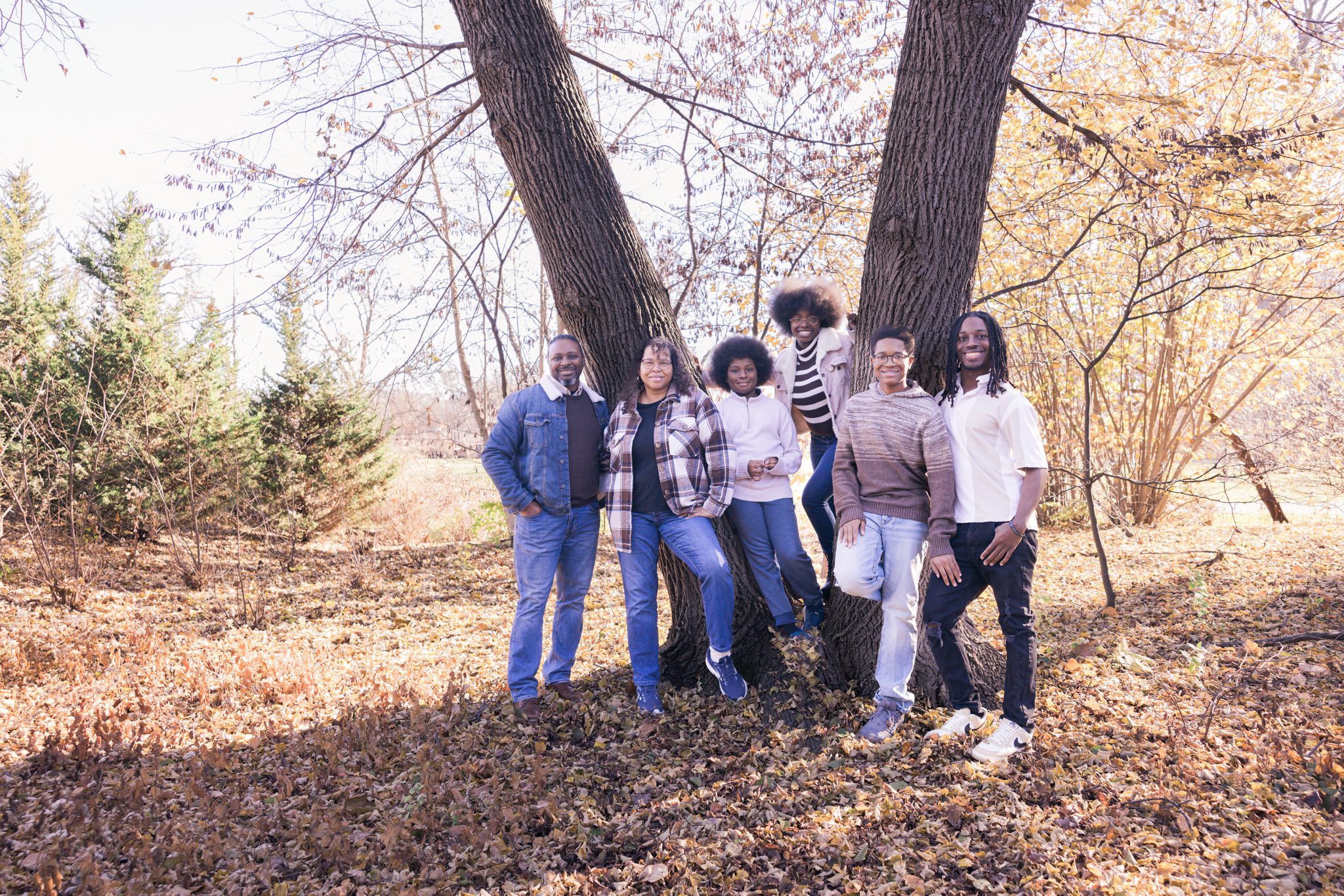 Mom and dad with their four grown children leaning up against a tree and smiling at the camera. Picture taken at Cantigny in Wheaton, IL