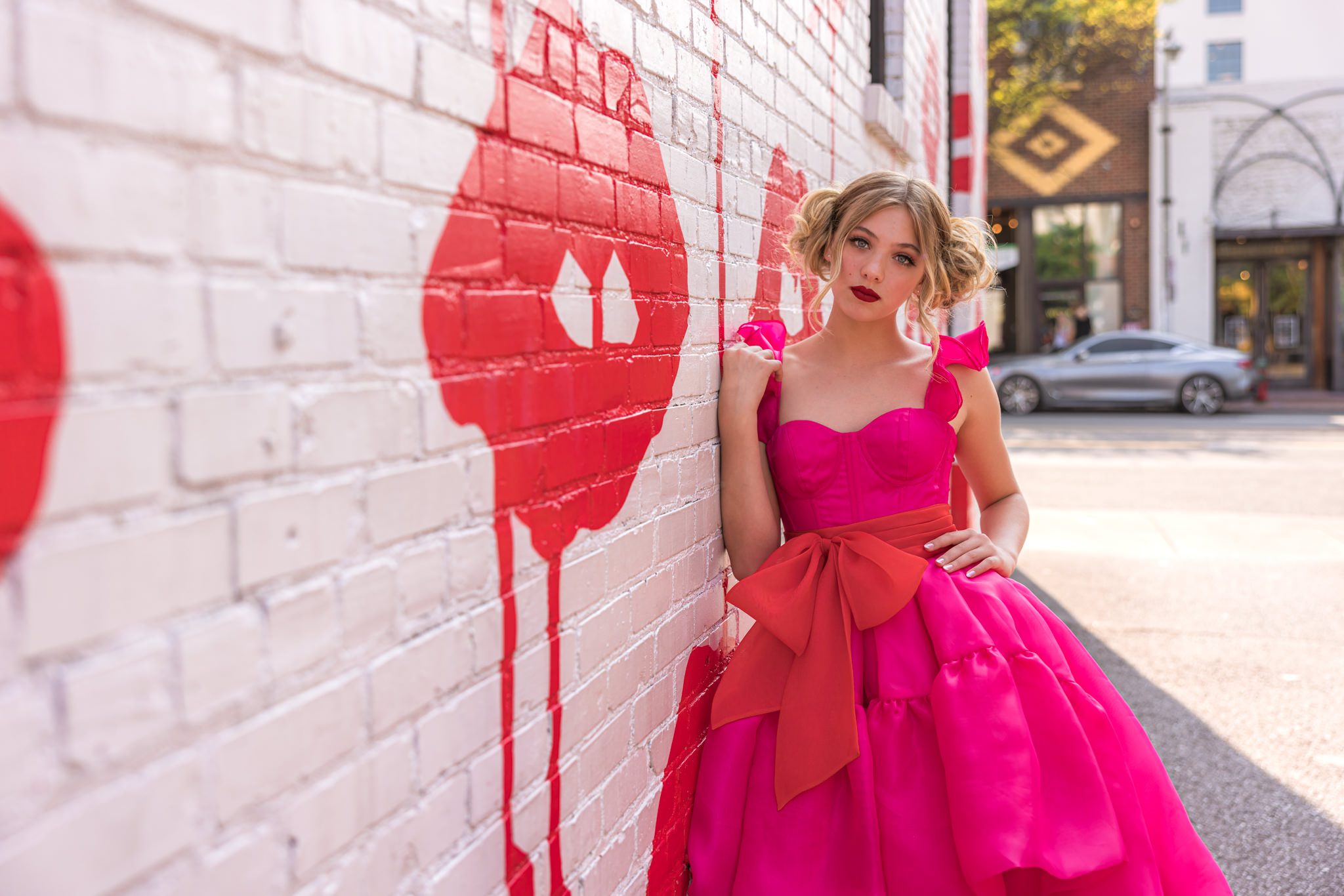Girl in pink and red dress leaning up against a wall that has red drippy lips on it.