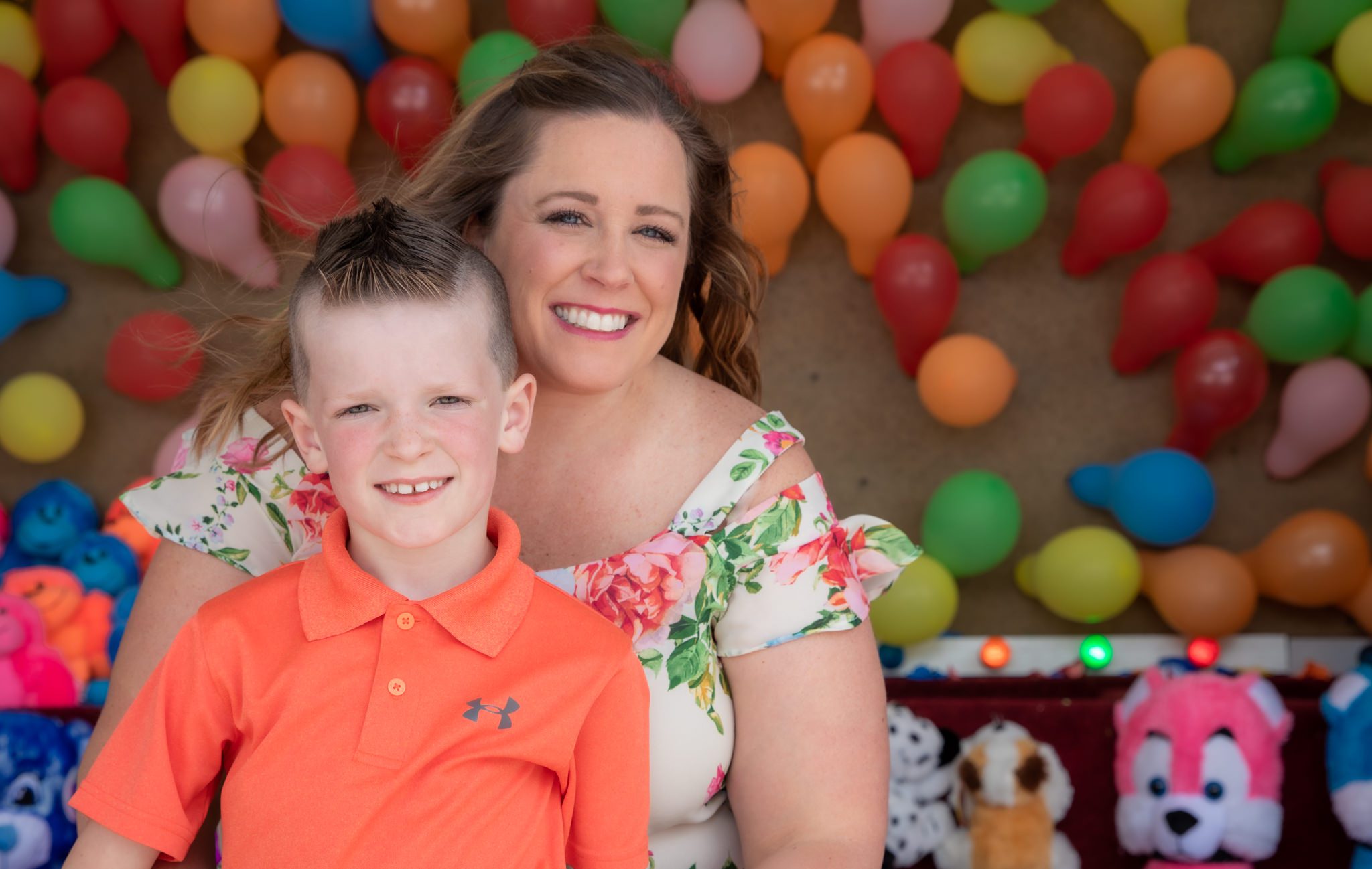 Young boy and his mom in front of a wall of balloons at a carnival